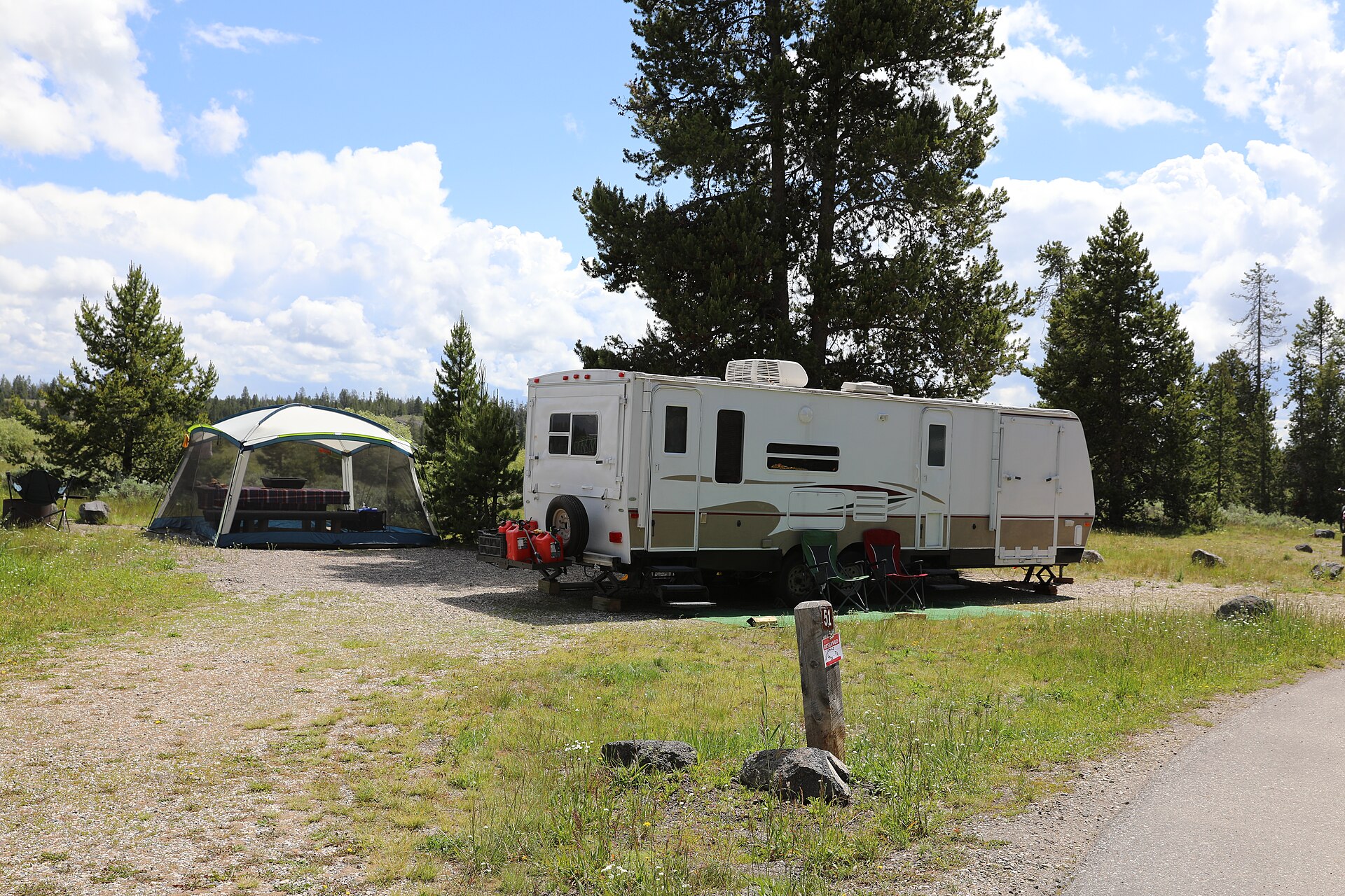 A travel trailer and screen shelter set up on a gravel pad at a forested campsite.